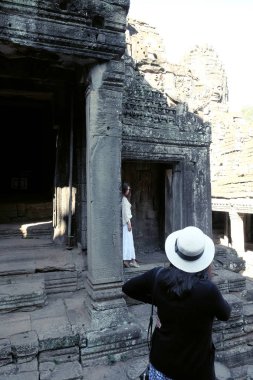 Siem Reap, Kamboçya, 18 Aralık 2018 Beyaz şapkalı ve siyah kazakgiyen bir kadın antik harabelere bakıyor. Bir kadın fotoğrafçı için poz kız inceliyor.