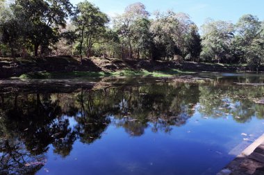 İnsan yapımı göl, kıyı ve alt taş kaplıdır. Antik Khmer rezervuarı. Baray, ne oldu? Göletin etrafında büyüyen ağaçlar, suya yansıdı.