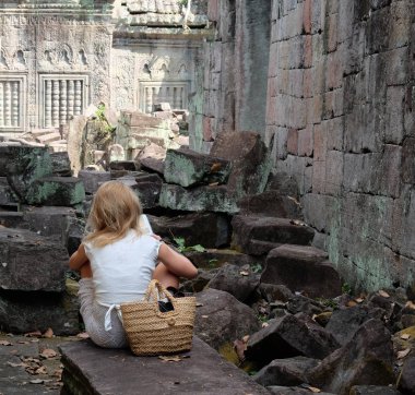 Genç sarışın bir kız bir taşın üzerine oturur ve bir kitap okur. Antik kalıntılar arasında gezgin. Şık bir saman torbası ile Kafkas kız.