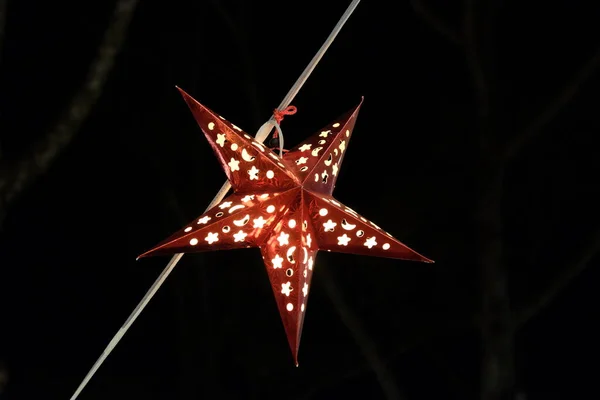 A decorative red star hangs on a metal cable. Decorative lantern in the shape of a star.