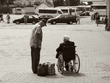 Chernihiv, Ukrayna, 7 Haziran 2019. Bir tren istasyonu çalışanı tekerlekli sandalyedeki yaşlı bir adamla iletişim kuruyor. Engelli yolculara yardım. Siyah ve beyaz.