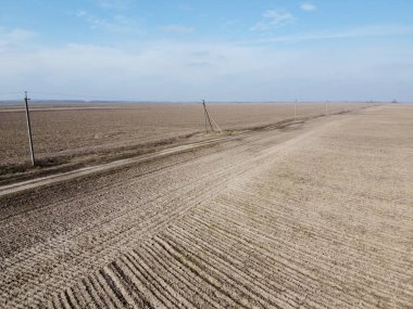 Tarlalar arasındaki toprak yol, hava manzarası. Manzara. Baharda ekilebilir tarlalar. Güç hattı direkleri.