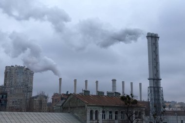 Duman çatıların üstündeki endüstriyel bacalardan geliyor. Gökyüzü gri bulutlarla kaplı. Çevre kirliliği.