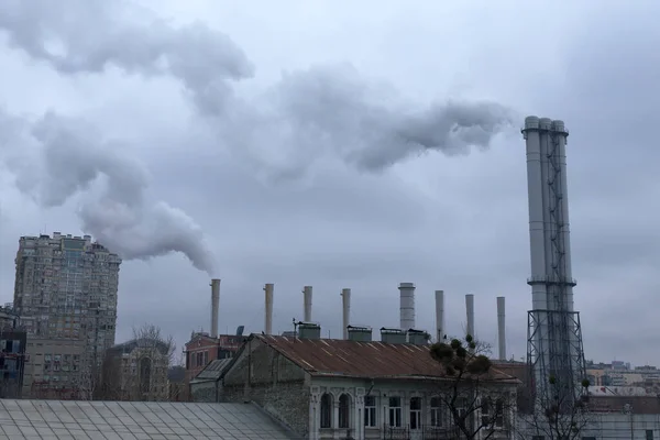 Duman çatıların üstündeki endüstriyel bacalardan geliyor. Gökyüzü gri bulutlarla kaplı. Çevre kirliliği.