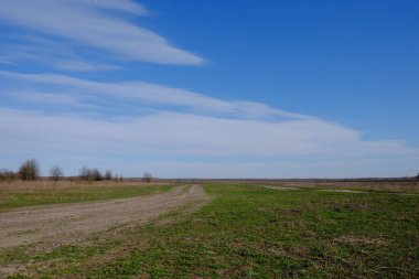 Bir bahar günü tarlalarda toprak yol. Kır manzarası. Güzel bulutlu gökyüzü tarlanın üzerinde.