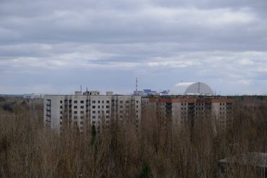 Pripyat 'ta terk edilmiş evler. Arka planda Çernobil nükleer santrali ve koruyucu lahit var..
