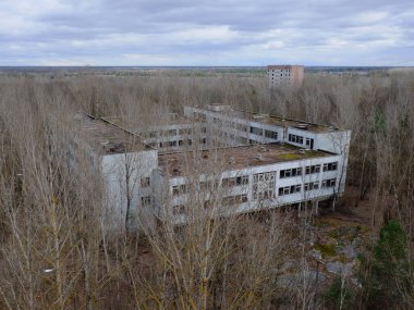 Pripyat 'taki ağaçların arasında terk edilmiş bir beton bina. Hava görüntüsü. Bulutlu hava, manzara.