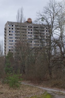 Pripyat 'ın hayalet kasabasında terk edilmiş bir ev. Ağaçlarla kaplı terk edilmiş bir şehir. Bölge radyasyonla kirlenmiş. Sovyet cumhuriyetinin arması binanın çatısında..