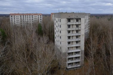 Pripyat 'ta yapraksız ağaçların arasında terk edilmiş paneller. Şehrin üzerinde güzel bulutlu bir gökyüzü. Sovyet sonrası mimarisi.
