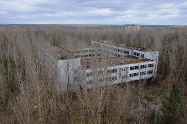 Pripyat 'taki ağaçların arasında terk edilmiş bir beton bina. Hava görüntüsü. Bulutlu hava, manzara.