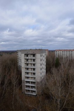 Pripyat 'ta yapraksız ağaçların arasında terk edilmiş paneller. Şehrin üzerinde güzel bulutlu bir gökyüzü. Sovyet sonrası mimarisi.