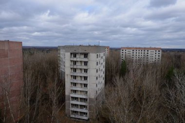 Pripyat 'ta yapraksız ağaçların arasında terk edilmiş paneller. Şehrin üzerinde güzel bulutlu bir gökyüzü. Sovyet sonrası mimarisi.