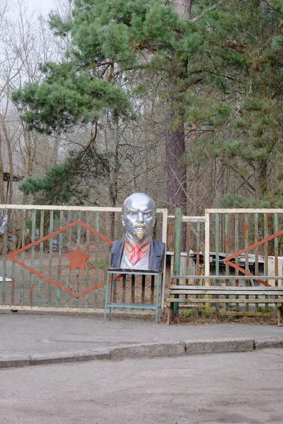 Painted bust of Lenin near a metal fence.