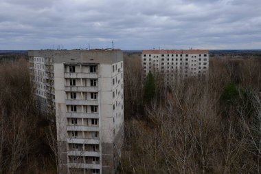 Pripyat 'ta yapraksız ağaçların arasında terk edilmiş paneller. Şehrin üzerinde güzel bulutlu bir gökyüzü. Sovyet sonrası mimarisi.