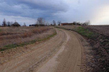 Gece tarlasında köy yolunda bir viraj. Alacakaranlık manzarası. Dramatik bulutlu gökyüzü.