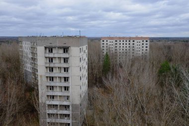 Pripyat 'ta yapraksız ağaçların arasında terk edilmiş paneller. Şehrin üzerinde güzel bulutlu bir gökyüzü. Sovyet sonrası mimarisi.