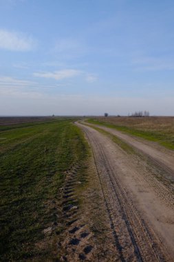 Akşam tarlasında dar bir toprak yol. Açık mavi gökyüzü tarlanın üzerinde.