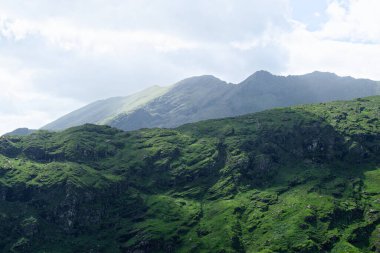 Yazın bulutlu bir günde İrlanda 'nın Kerry ilçesindeki Dunloe geçidinde yeşil yosunlarla kaplı tepeler..