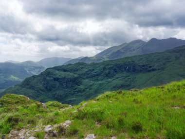 Kerry County 'de bulutlu bir gökyüzünün altında yuvarlanan yeşil tepeler ve dağ tepeleri görülebilir. Ön planda canlı yeşil çimenler var. Güzel bir İrlanda manzarası yaratıyor..