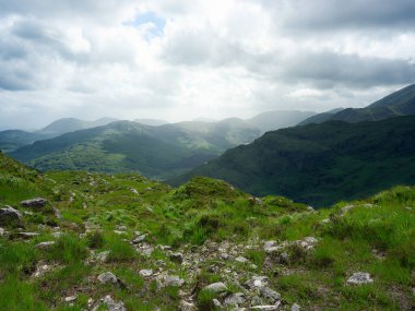 Bulutlu bir günde yeşil dağlar ve bir vadi bir gözden görülebilir. Güneş, İrlanda 'daki Dunloe Geçidi' nin bulutları arasından parlıyor..