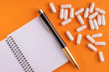 Tıbbi kapsül ve hapları boş bir defter kalem bir turuncu arka plan, yakın çekim, kopya alanı ile üstten görünüm ile çevresinde.