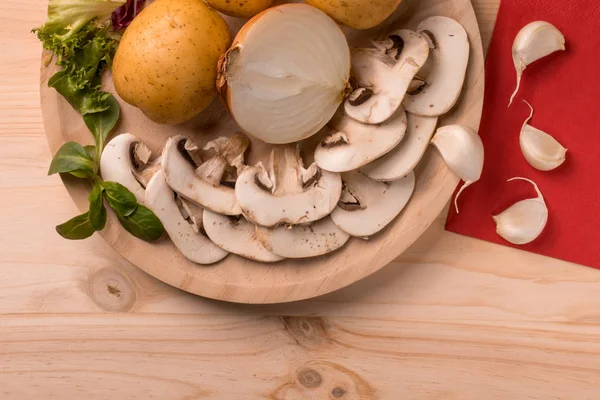 Appetizing products for cooking, mushrooms, potatoes, onions, garlic, herbs on a wooden background with kitchen utensils. Place for inscriptions.
