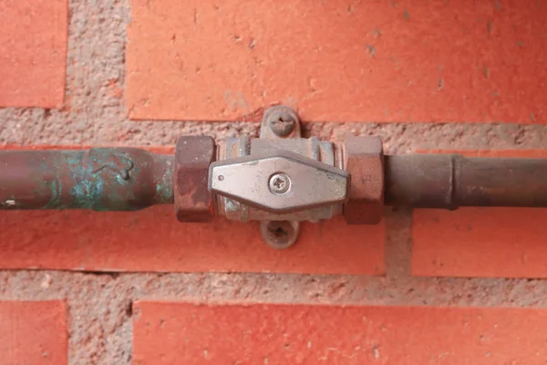 Gas pipes and valve in the open position against a red brick wall