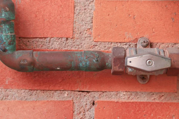 Gas pipes and valve in the open position against a red brick wall