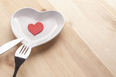 Kırmızı kalp şeklinde bir kalp bir çatal ve bıçak ahşap bir zemin üzerine beyaz bir tabakta. Sevgililer günü ve anneler günü Festival arka plan