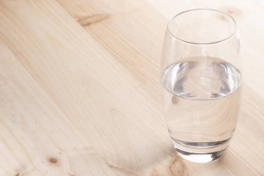 Image of a half full glass of water standing on a wooden table clipart