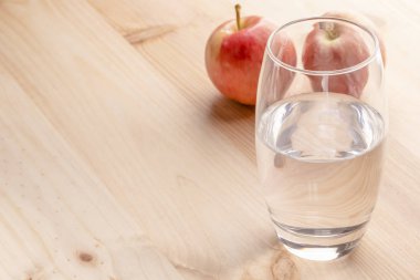 Bir bardağı ahşap bir masa üzerinde duran su dolu bir görüntü arka planda elmalar vardır. Sağlıklı beslenme ve kilo kaybetme kavramı