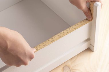 Genç bir adam bir başucundaki kat etmeye çalışıyor. Bu raflar bir ölçme aracı ile ölçer.