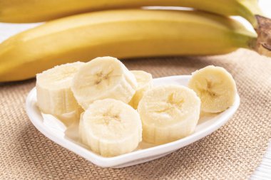 Dilimlenmiş ve tüm muz beyaz kalp şeklindeki plaka ve güneş ışınlarının bir eski ahşap tablo