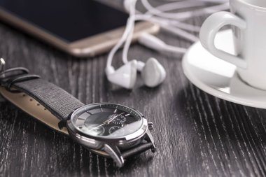 Kol saati ve bir fincan kahve koyu ahşap bir masa üzerinde ve kulaklık ile cep telefonu. İş yemeği ve öğle yemeği molası iş kavramı