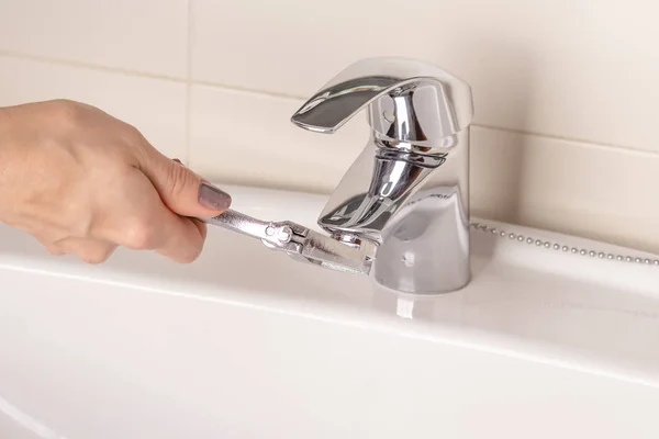 Vinç aerator tamiri. Banyo mikser parçalara ayırma. Kızın elini bir manikür ile döner ve mekanizması ayarlanabilir bir anahtarı ile detayını katlanmış