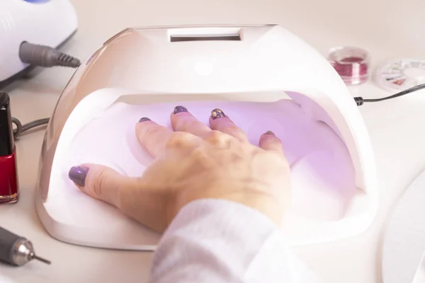 Bir kızın elini oje dosyalar ve portakal sopa Rhinestones bir manikür tabloda salonda bir ultraviyole çivi LAMP