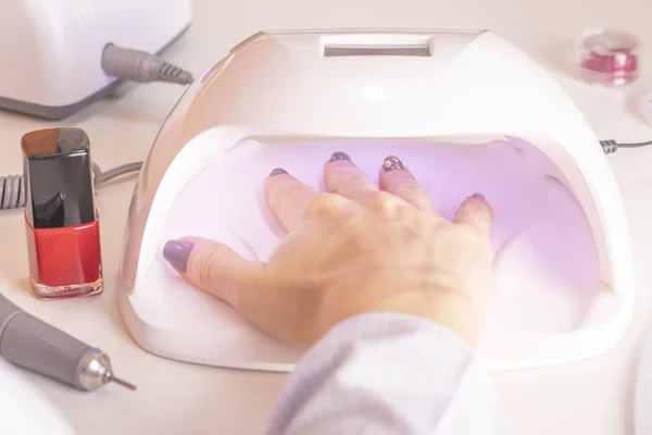 A girl\'s hand in an ultraviolet nail lamp with nail polish files and orange sticks of rhinestones on a manicure table in the salon