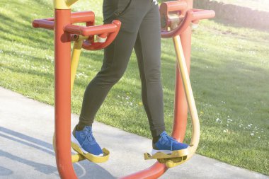 Genel bir parkta egzersiz donanımları ile eğitim genç kadın. Beyaz çiçekli arka plan yeşil çim. Spor ve fitness yardımıyla ince bir rakam sürdürmek kavramı