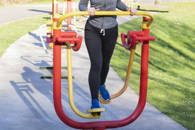 Genel bir parkta egzersiz donanımları ile eğitim genç kadın. Beyaz çiçekli arka plan yeşil çimen.