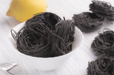 Siyah beyaz masa arka plan üzerinde beyaz bir tabak makarna. Kavram sıradan yemekler değil. Makarnalık buğday mürekkep balığı mürekkeple yapılmış. Limon ve çatal ile tamamlamak