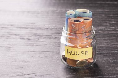 Cam Kavanoz sikke ve siyah ahşap bir masa üzerinde kelime House Notes'la euro ile. Tamir, ev giderleri inşaatı için mali tasarruf kavramı.
