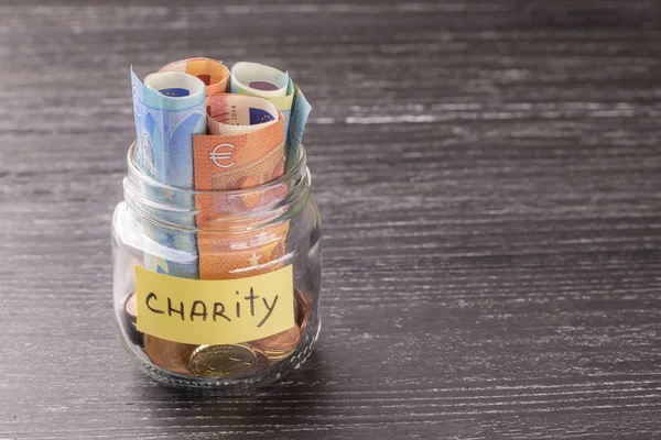 Cam Kavanoz sikke ve yazıt sadaka Notes'la euro ile. Eski siyah ahşap masanın üstünde. İyilik ve yardım kavramı.