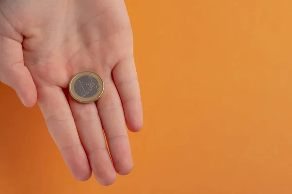Turuncu bir arka plan üzerinde bir çocuk gencin elinde 1 euro para.