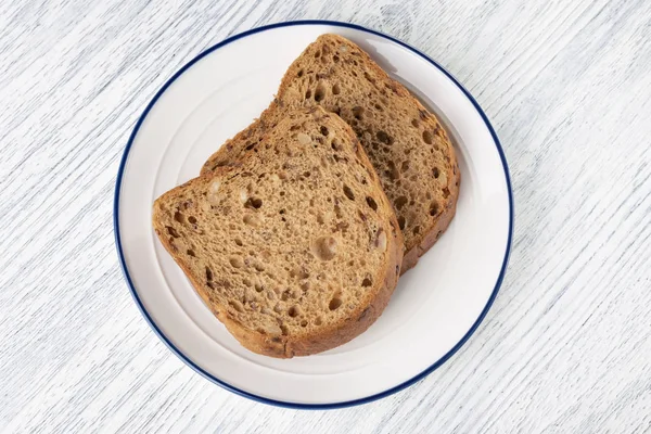 Rebanadas de pan de grano con moho. En un plato blanco con una raya azul. Sobre una mesa de madera — Foto de Stock