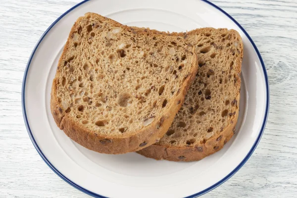 Rebanadas de pan de grano con moho. En un plato blanco con una raya azul. Sobre una mesa de madera — Foto de Stock