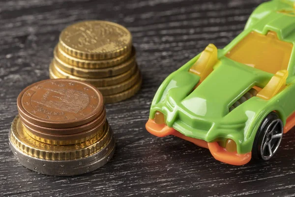 Car toy and euro coins on a dark wooden background.