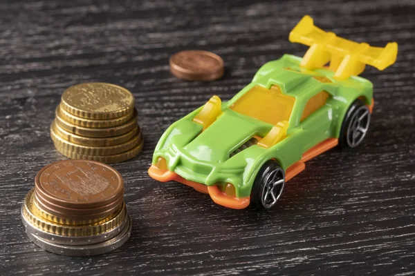 Car toy and euro coins on a dark wooden background.