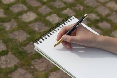 Parkta açık bir not defteri üzerinde bir kalem ile çocuk eli.
