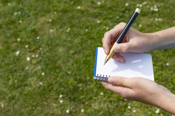 Mano del ragazzo con una matita sopra un blocco note aperto nel parco . — Foto Stock