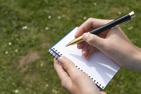 Το χέρι του αγοριού με ένα μολύβι πάνω από ένα ανοιχτό σημειωματάριο στο πάρκο. — Φωτογραφία Αρχείου